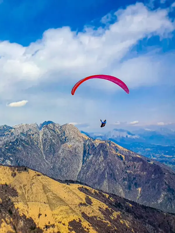 Paragliding pilots fly over the green hills and rocky mountains of Bassano del Grappa on an Easter excursion with touch and go Paragliding.