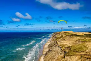 Paraglider pilots soaring and groundhandling on the dunes of Lökken with a view of the iconic lighthouse.
