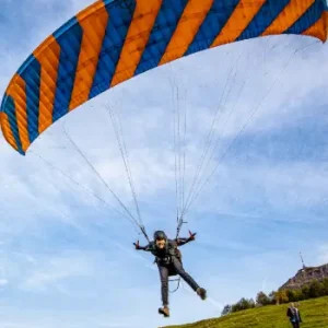 Ein Schüler hebt mit einem Phi-Gleitschirm ab und startet seinen ersten kleinen Flug am Übungshang unter Anleitung eines erfahrenen Fluglehrers.