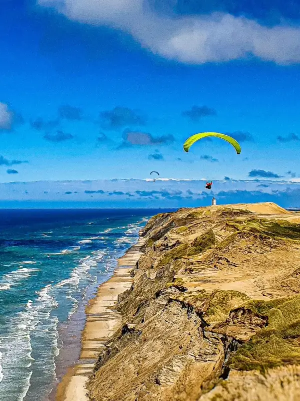 Paraglider pilots soaring and groundhandling on the dunes of Lökken with a view of the iconic lighthouse.