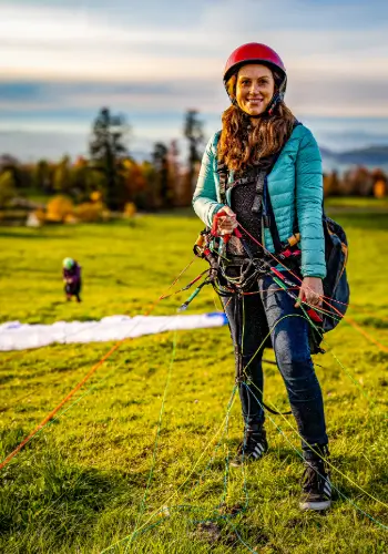 A paragliding student is ready to take off on the practice slope, accompanied by an experienced instructor.
