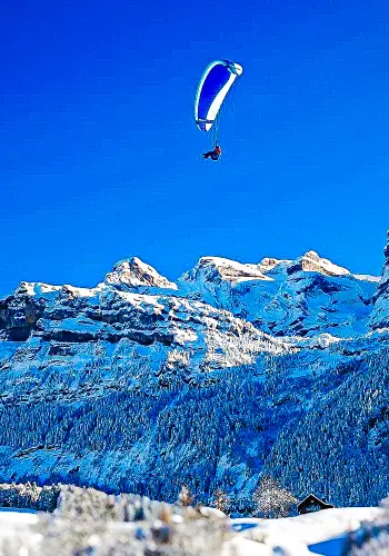 Ein Schüler fliegt mit seinem Nova Gleitschirm über die malerische Landschaft von Wolfenschiessen während eines Trainingflugs.