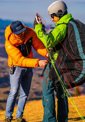 Paragliding students at the launch site while the instructor carefully checks the equipment and lines to ensure a safe launch.