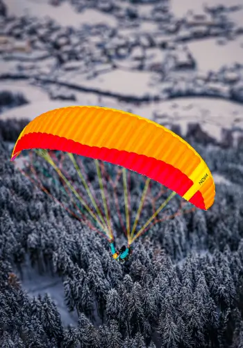 A paraglider pilot flies over snow-covered forests in central Switzerland and enjoys the wintry landscape from a bird's eye view.