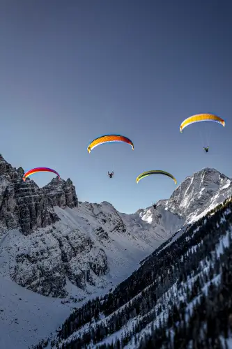 Four paragliders fly in front of the majestic Alpine backdrop during a paragliding experience with touch and go paragliding.
