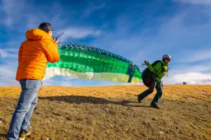 Paragliding student with green Nova paraglider at the start, supported by an experienced instructor in central Switzerland.