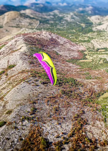 Paraglider pilot soars over the picturesque hills of Bosnia during the Bosnia tour of touch and go paragliding.