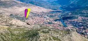 Paraglider pilot soars over the picturesque hills of Bosnia during the Bosnia tour of touch and go paragliding.