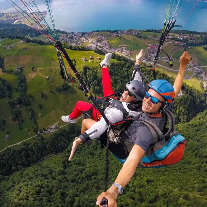 Tandempilot mit Passagierin beim Gleitschirmflug über der beeindruckenden Berglandschaft und Seen der Zentralschweiz, umgeben von klarer Luft und atemberaubender Aussicht.