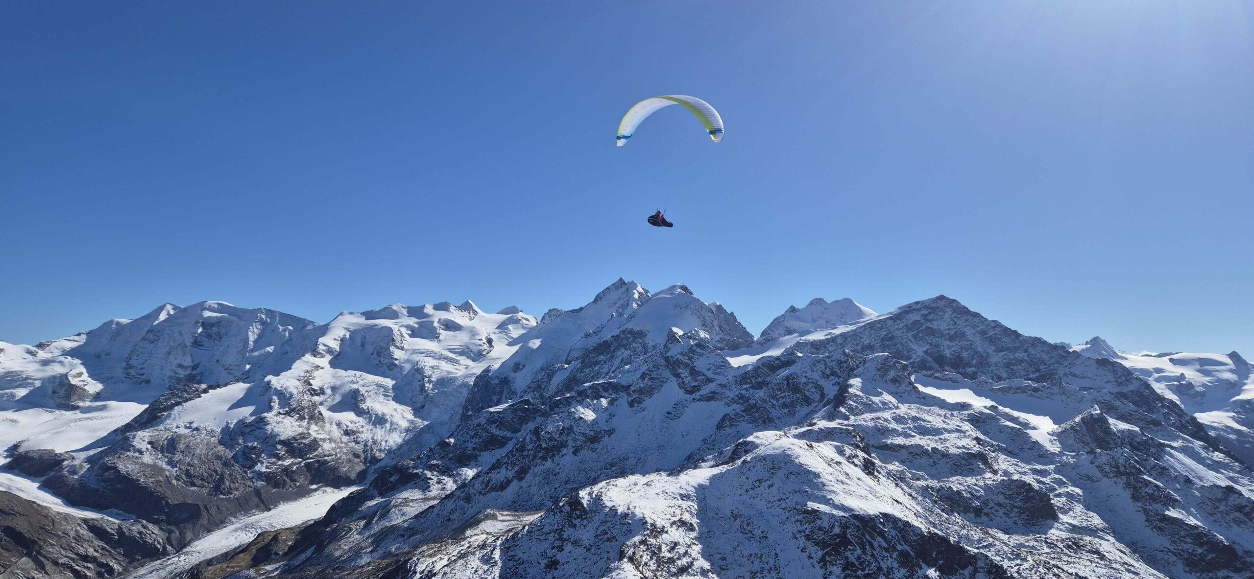 Paraglider pilot flies over the Engadine mountains with a wide view of the alpine landscape.