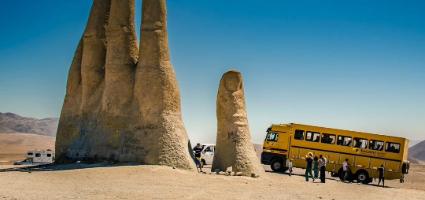 Touristenbus vor einer grossen Steinhände-Skulptur, die als Sehenswürdigkeit dient