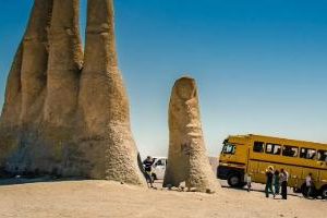 Touristenbus vor einer grossen Steinhände-Skulptur, die als Sehenswürdigkeit dient